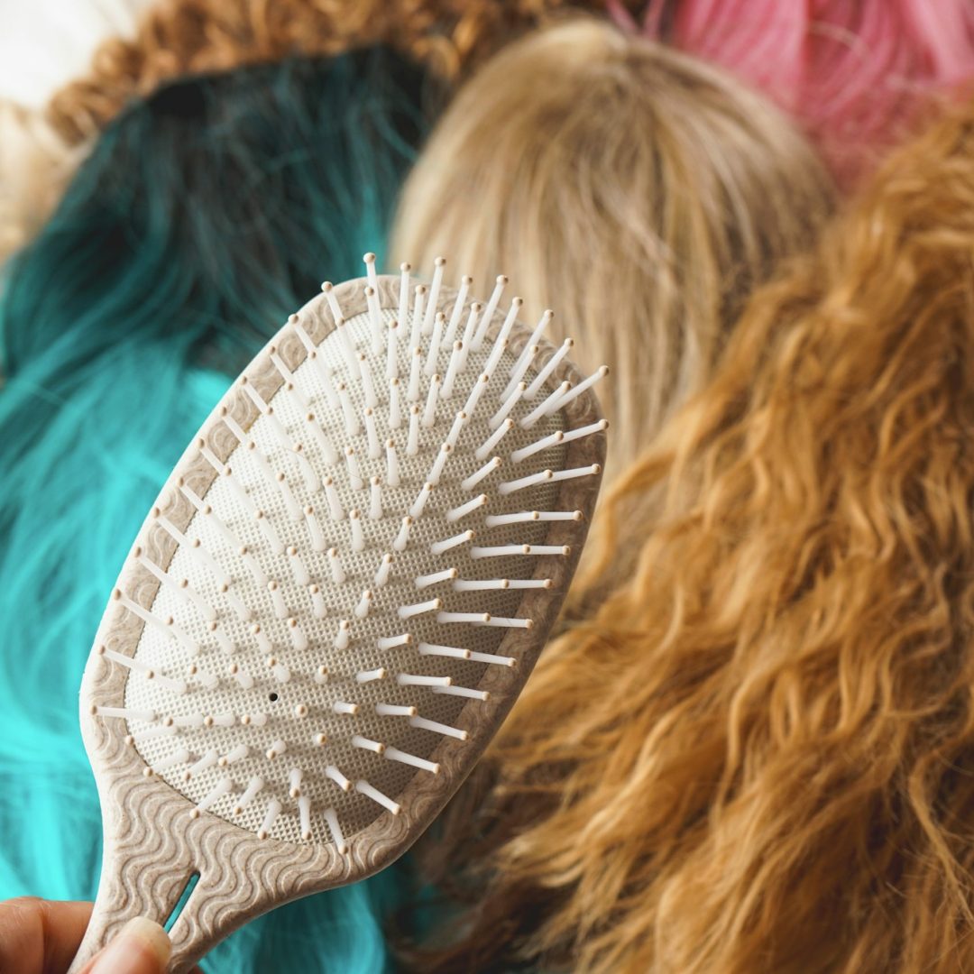 Close up of a hair brush against a background of a lot of wigs